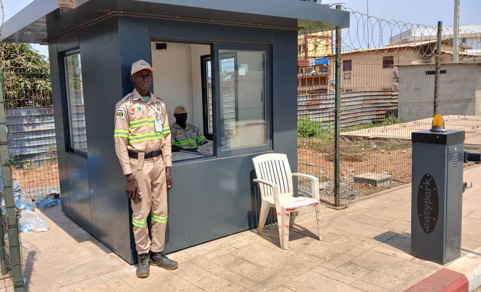 Security team briefing at construction site perimeter, low industrial lighting, guards in uniform, dark steel environment