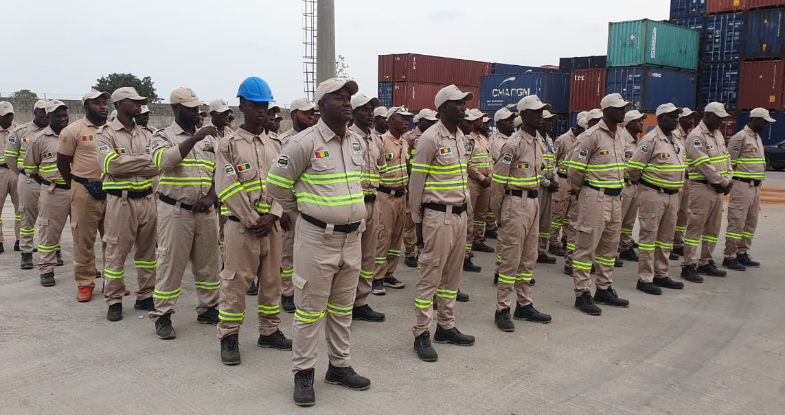 Security personnel in dark tactical gear standing guard at industrial site entrance at night, deep shadows, dim perimeter lighting